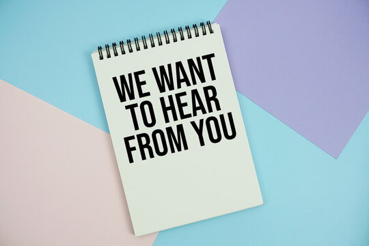 We Want To Hear From You text written on notepad flat lay on multicolor pastel background