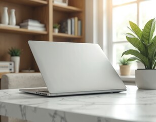 Fototapeta premium Modern silver laptop rests on white marble table. Bookshelf plant and window provide natural light for bright, clean home office workspace. Tech setup offers calm work environment.