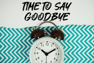 Fototapeta premium Time To Say Goodbye text written on paper rip with alarm clock flat lay on turquoise chevron background