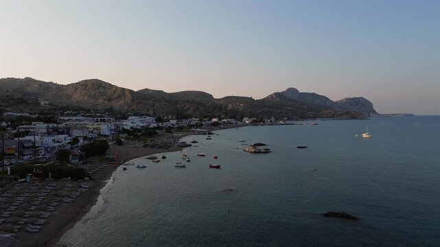 Cinematic high-angle drone shot of Stegna Beach in Rhodes. Stunning panoramic view of turquoise waters, beach umbrellas, and traditional white buildings. Ideal for travel storytelling