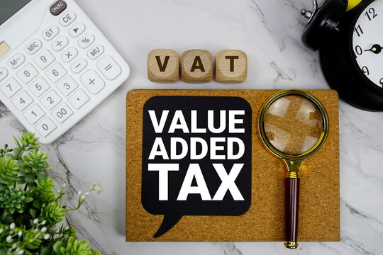 VAT Value Added Tax text with calculator, magnifying glass and alarm clock on marble background