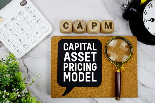 CAPM Capital Asset Pricing Model text with calculator, magnifying glass and alarm clock on marble background