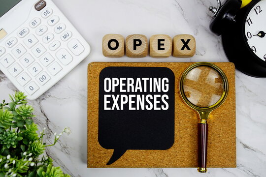 OPEX Operating Expenses text with calculator, magnifying glass and alarm clock on marble background