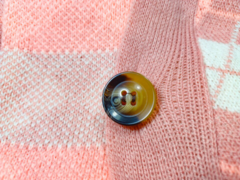 Close-up of a brown marble button on a pink knitted cardigan. Detail of clothing accessory on soft argyle fabric. Elegant garment element and fashion texture.