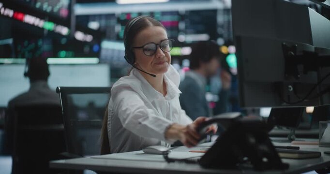 Professional Woman Trader in Glasses in High Intensity Office, Handling Business Call on Stationary Phone While Analyzing Complex Real Time Charts on Large Monitors. Professional Communication.