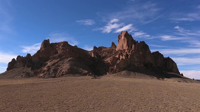 A cinematic drone approach moves toward sharp volcanic mountain spires and jagged rock formations, showcasing the dramatic geological verticality and vastness of the arid desert wilderness.