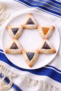 Traditional triangular hamantaschen cookies dusted with powdered sugar, filled with poppy seed and apricot jam, arranged on a white plate, top view food photography.