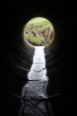 Fototapeta premium View through a round concrete tunnel carrying a stream beneath a road