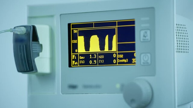 Vital signs monitor displaying waveform readings in operating room with sunlight.