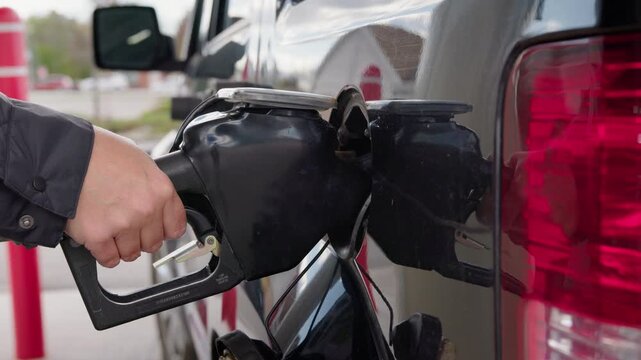 Driver refueling car at gas station and finishing fueling process reflecting 