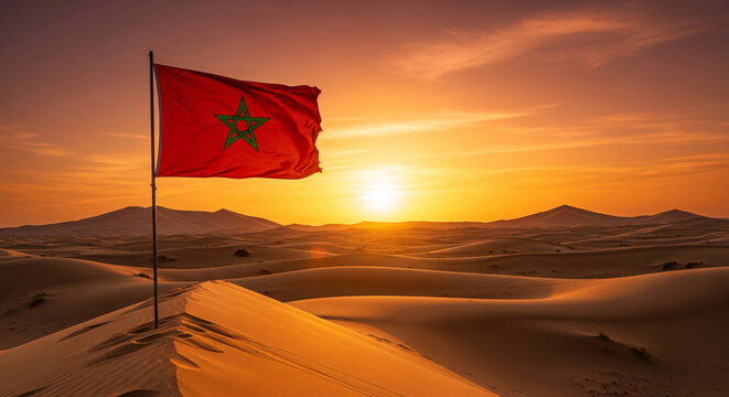 Red Moroccan Flag With A Green Pentagram Waving On A Pole Atop A High Sand Dune In The Sahara Desert During A Dramatic Sunset With Mountains In The Distance And Orange Clouds In The Sky