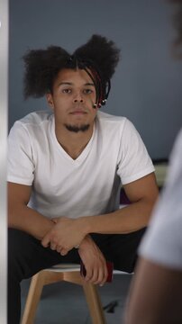 Confident young man with mixed-race ethnicity sitting in front of the mirror, appreciating his afro dreadlocks hairstyle during his daily routine