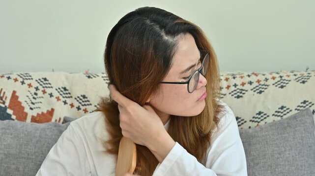 Asian woman having problem of her thick hair while brushing her. Thick hair weights more than thin hair and prone to damage and frizzy.