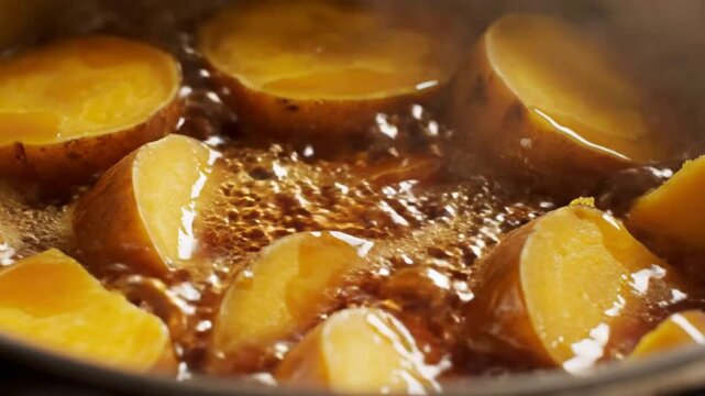 Close-up of golden sweet potatoes boiling in a metal pot with bubbling liquid on a stovetop.