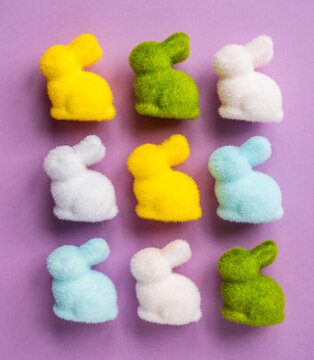 Top view of many colorful fuzzy Easter bunnies on purple background.