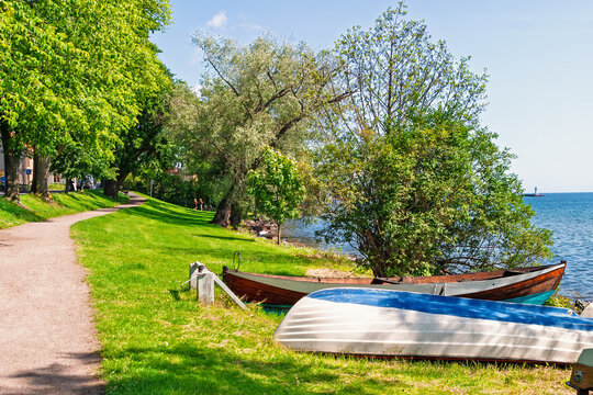 Lakeside path with boats and distant lighthouse on a sunny summer day