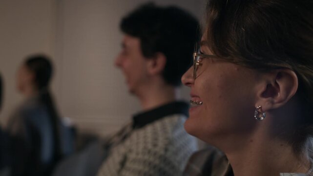 Rack focus of female stand up comedy fan with braces laughing during comedians performance on stage while sitting in audience seats next to cheering crowd, slow motion