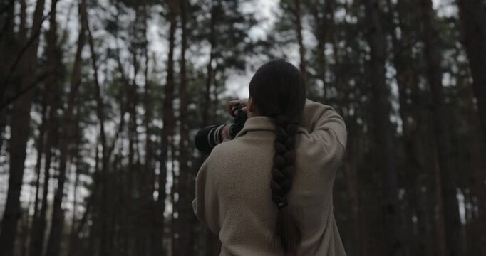 Female photographer with professional camera and telephoto lens in a pine forest