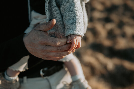 Gros plan d'une main d'adulte tenant d&eacute;licatement la main d'un petit enfant