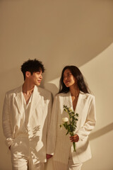 Young couple in white suits sharing a loving glance, celebrating romance and partnership with flowers