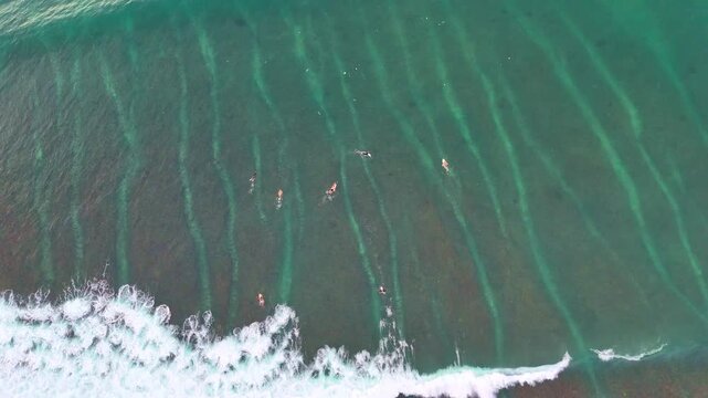 Aerial drone shot flying parallel to surfers riding waves near dramatic rocky cliffs in Bali, Indonesia. Dynamic action scene capturing the thrill of surfing in crystal clear ocean water