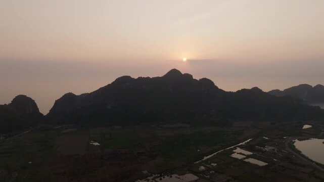 Cat Ba Vietnam aerial view of a road cutting through fields and wetlands beneath towering limestone karst at dusk.