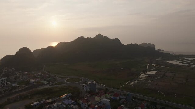 Cat Ba Vietnam aerial view of a curving road and small town beside karst hills and open fields at dusk.