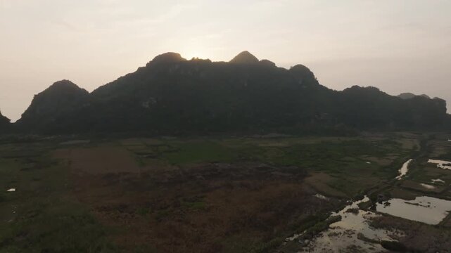Cat Ba Vietnam aerial tracking shot along a limestone karst ridge with wet fields and canals leading toward the coast.