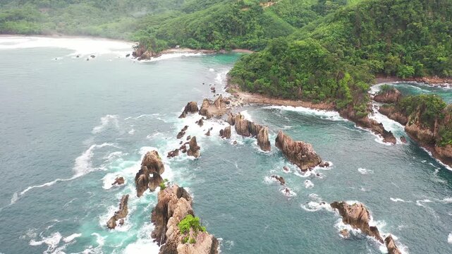 Drone shot of tropical coastline with rocky formations and clear blue ocean water.