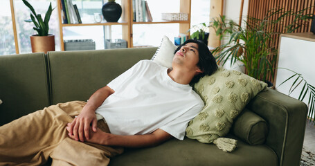 Obraz premium Thinking, sad and asian man relax on couch, introspection and self reflection for emotional processing. Rest, home and person with confirmation bias for experience memory, regret and remember mistake