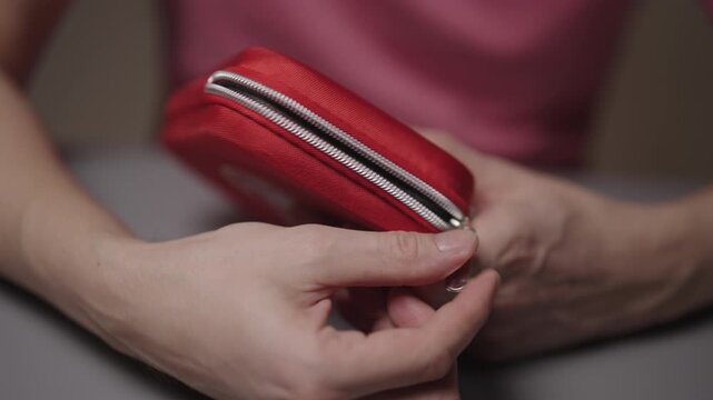 Close-up view of male hands opening and closing zipper of small red first aid kit, demonstrating importance of being prepared for medical emergencies and accidents. Shooting in slow motion.