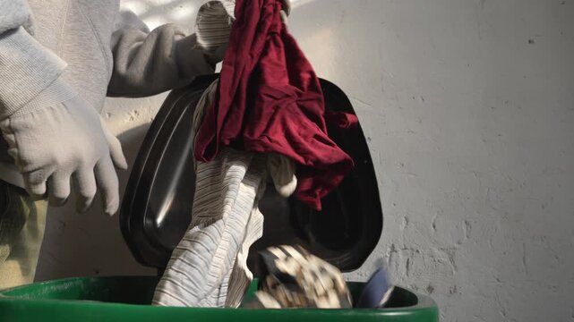 Man throwing old clothes into trash bin clothing waste concept. The problem of fast fashion, textile waste