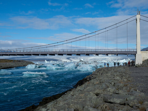 Visitors under the bridge carrying route 1 over Glacier Lagoon in Iceland with icebergs floating