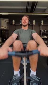 Authentic social media style smartphone POV video of a man around thirty rowing on a machine in a modern black minimalist gym, symbol of discipline, endurance, focus, strength and real fitness