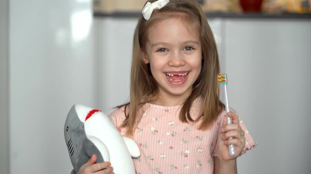 Portrait of little happy toothless girl with toothbrush looks at camera and laughs. Childrens oral hygiene. Baby milk teeth change