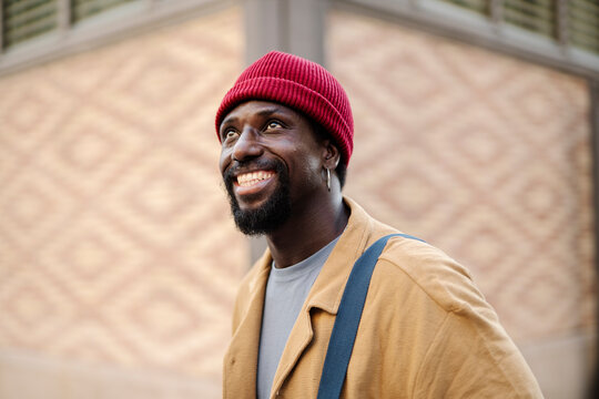 Smiling man in red beanie and autumn jacket outdoors in city