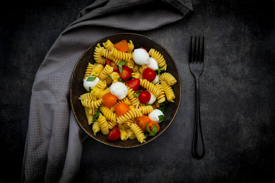 Fresh pasta salad with mozzarella tomato and basil in bowl overhead view