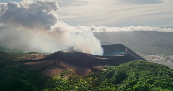 Mount Yasur, an active stratovolcano on Tanna Island, Vanuatu, continuously emits white smoke and ash from its crater, creating a dramatic natural landscape of lush tropical vegetation. Aerial shot
