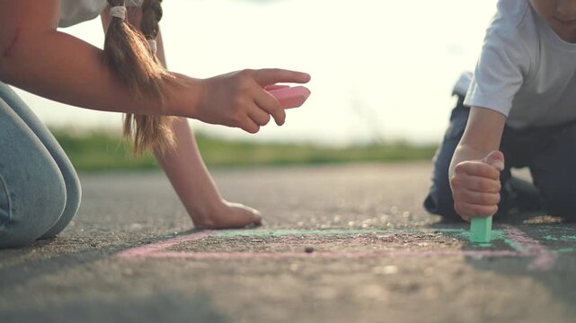 Kids, children, and their hands covered in chalk, drawing and playing on the street. Outdoor fun mixes art as children and kids turn plain street into a colorful and creative chalk outdoor creation.