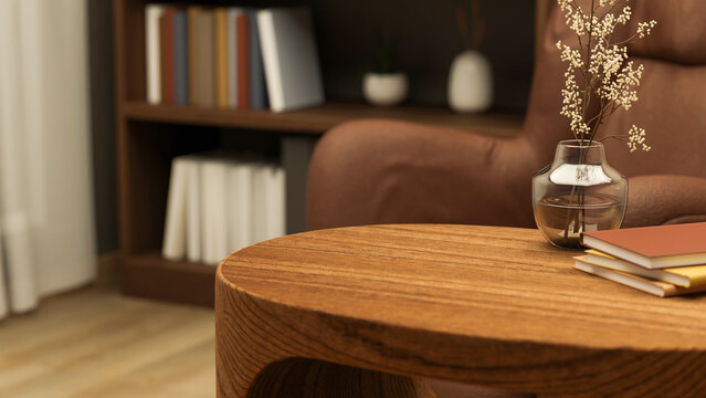 Books and glass flower vase on wooden table aside armchair and bookshelf in a living room or library
