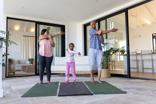 African American family stretching with child in sportswear on yoga mats on patio by sliding doors