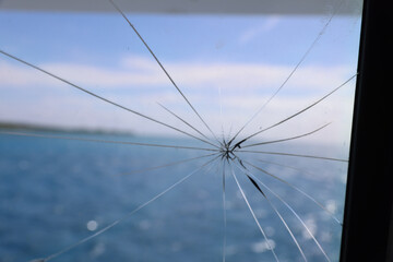 Fototapeta premium Spider Crack on Glass Window with Blue Ocean and Sky Background – Broken Glass Concept