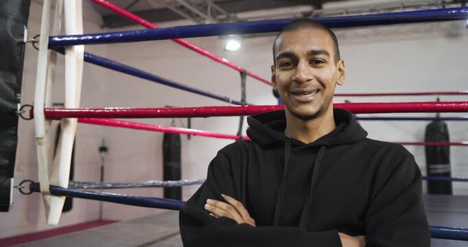 Camera pushing in while man crossing arms in boxing ring near punching bag flashing grin