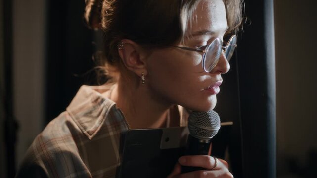 Tilt up shot of worried young adult female comedian with glasses peeking from behind curtain while waiting for turn to walk up on stage