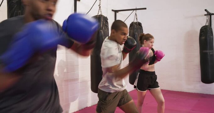 Diverse boxing trainees following teammate leading combos for workout, shadowboxing on pink mat