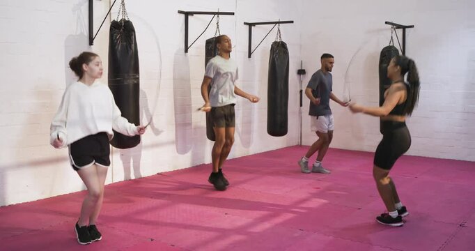 Diverse friends responding to start cue, skipping rope together in gym studio, camera narrowing