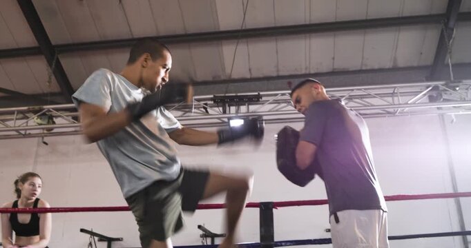 Male trainee boxer following trainer cue, delivering combo and kick on mitts for training in ring