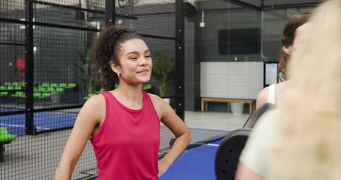 Diverse female friends in sportswear catching lobbed ball, swapping rackets on blue court for rally