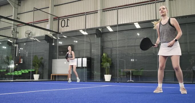 After toss, two women athletes practicing on court, rallying ball with paddles and high fiving