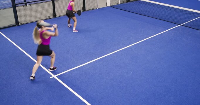 Diverse female teammates returning green ball on blue court, forcing high return, winning point